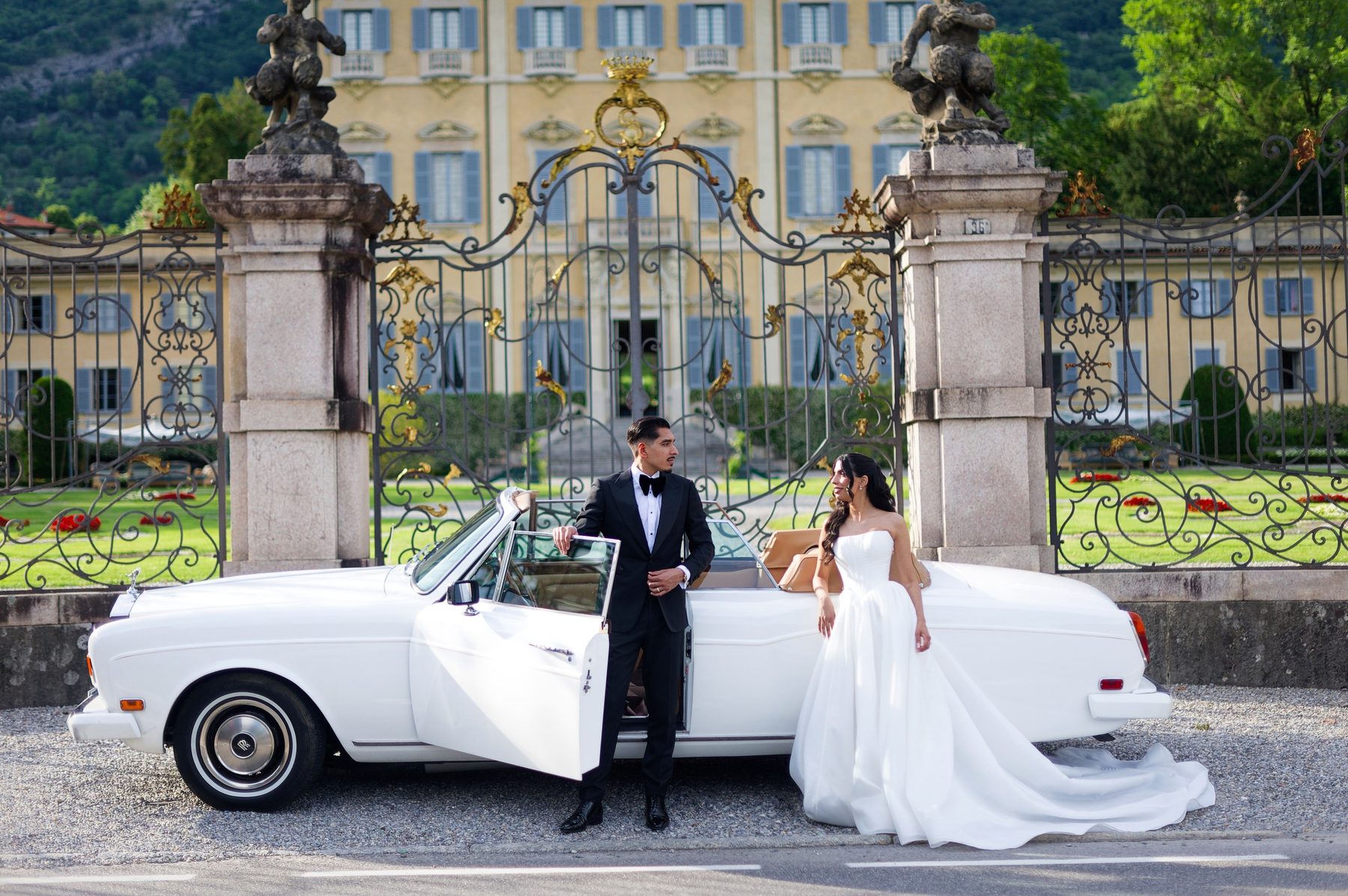 The couple arriving at the villa gates beside a white classic car